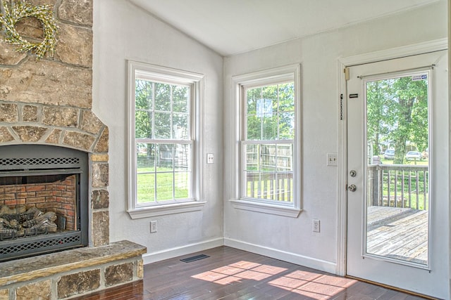 doorway with visible vents, baseboards, dark wood-type flooring, a stone fireplace, and lofted ceiling