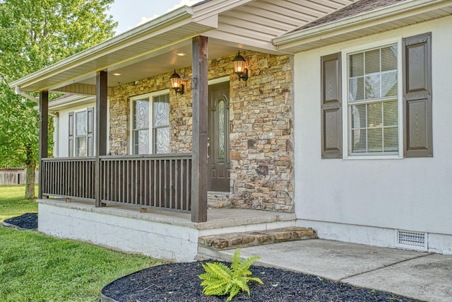 view of exterior entry with covered porch, crawl space, stone siding, and visible vents