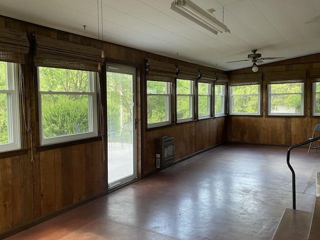 unfurnished sunroom with concrete floors, plenty of natural light, wooden walls, and heating unit