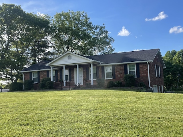view of front of property featuring covered porch, roof with shingles, brick siding, and a front yard