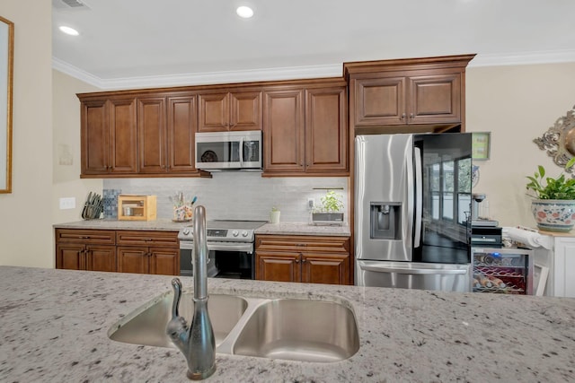 kitchen with brown cabinets, crown molding, light stone countertops, appliances with stainless steel finishes, and decorative backsplash