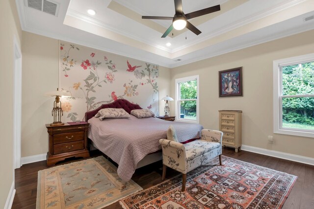 bedroom with ornamental molding, visible vents, dark wood-style flooring, a tray ceiling, and baseboards