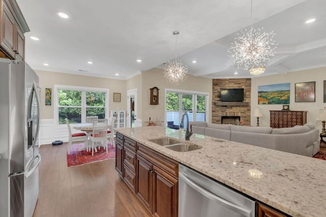 kitchen with an inviting chandelier, a sink, a fireplace, appliances with stainless steel finishes, and light stone counters