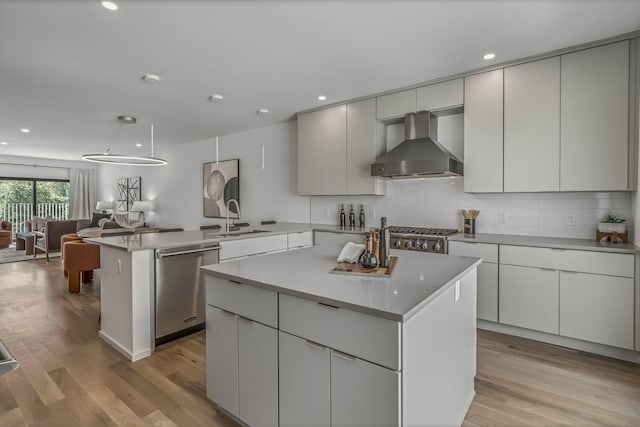 kitchen with a peninsula, stainless steel appliances, wall chimney range hood, open floor plan, and a kitchen island
