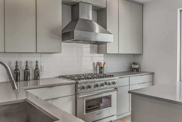 kitchen featuring high end stainless steel range oven, modern cabinets, tasteful backsplash, and wall chimney exhaust hood