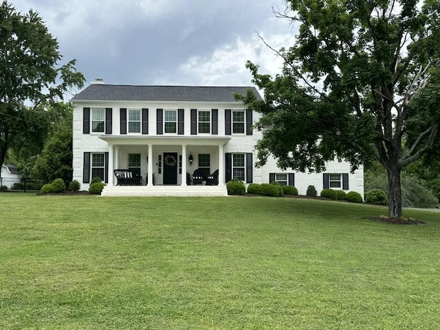 colonial inspired home with a porch, a front lawn, and a chimney