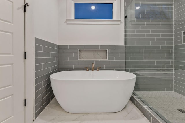 bathroom with tile walls, tiled shower, marble finish floor, and a freestanding tub