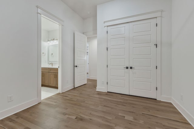 unfurnished bedroom featuring light wood finished floors, ensuite bathroom, a closet, and baseboards