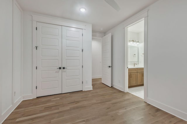 unfurnished bedroom featuring a sink, ensuite bathroom, a closet, light wood-style flooring, and baseboards