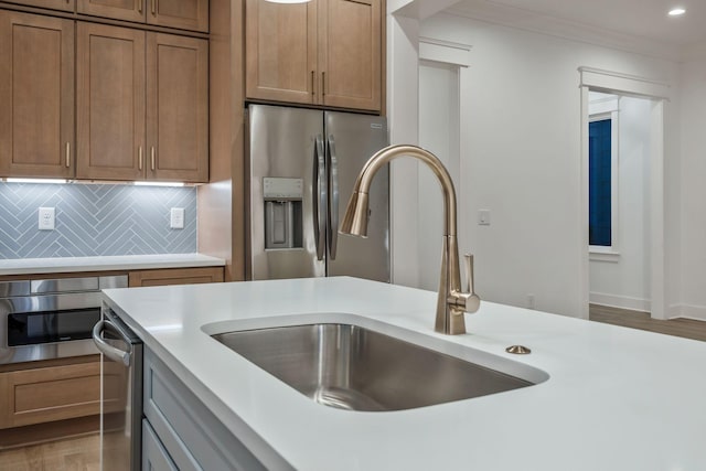 kitchen featuring light wood-style flooring, a sink, stainless steel appliances, backsplash, and light countertops