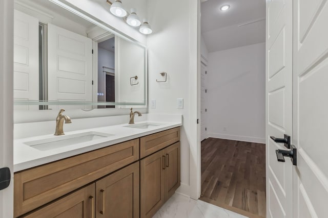 bathroom featuring double vanity, wood finished floors, baseboards, and a sink