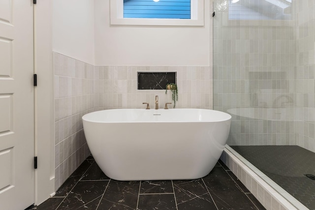 bathroom featuring marble finish floor, tile walls, tiled shower, and a freestanding tub