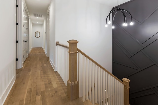 hallway with an upstairs landing, light wood-style flooring, and visible vents