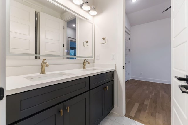 full bath with double vanity, wood finished floors, baseboards, and a sink