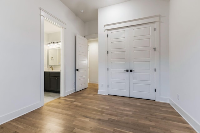 unfurnished bedroom with a sink, light wood-style flooring, a closet, and baseboards