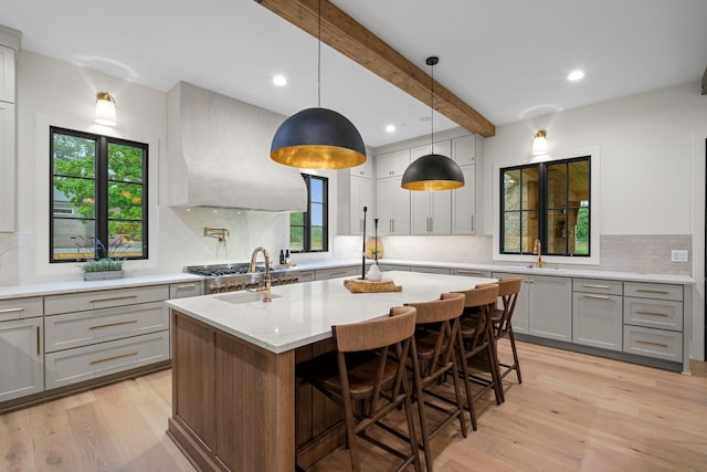 kitchen featuring light wood finished floors, a sink, gray cabinets, light stone countertops, and tasteful backsplash