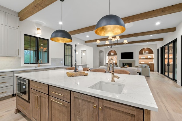 kitchen with a sink, beam ceiling, light wood-type flooring, a center island with sink, and open floor plan