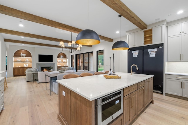 kitchen featuring recessed lighting, black refrigerator, a lit fireplace, light wood-style floors, and an island with sink