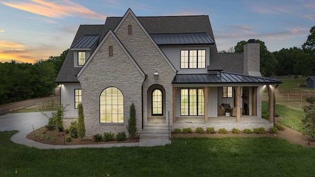 back of house with a lawn, covered porch, metal roof, and a standing seam roof