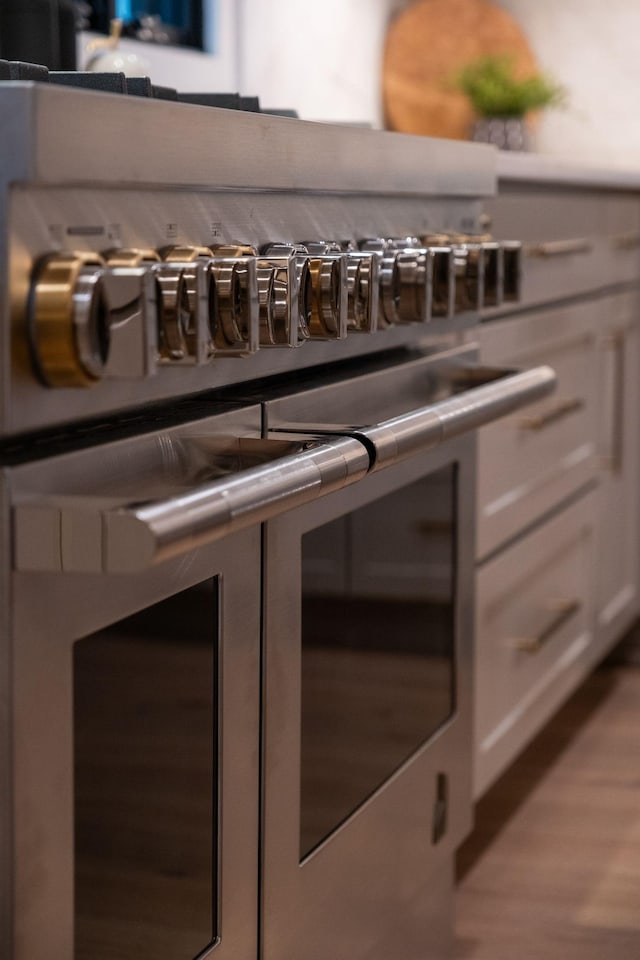 details featuring white cabinetry, double oven range, light countertops, and wood finished floors
