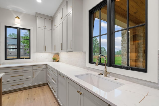 kitchen with a sink, light wood finished floors, backsplash, and light countertops
