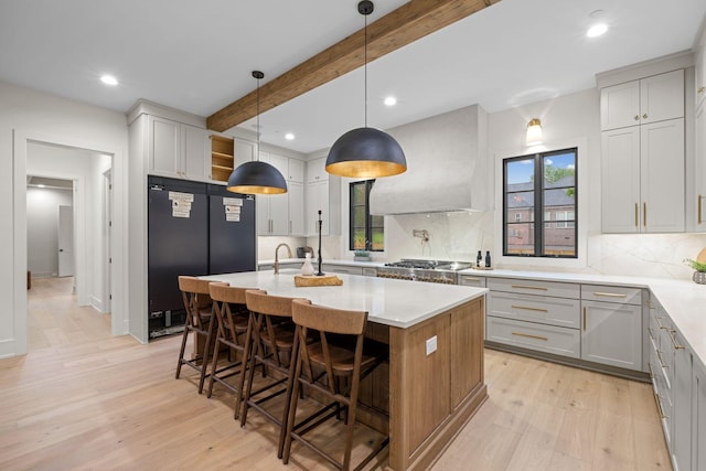 kitchen with tasteful backsplash, beam ceiling, stainless steel gas cooktop, black fridge, and light wood-style floors