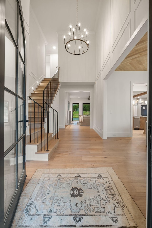 entrance foyer with baseboards, an inviting chandelier, stairs, a towering ceiling, and wood finished floors