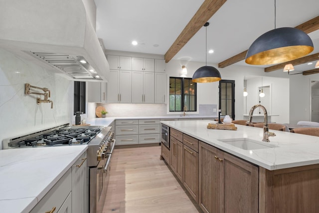 kitchen featuring light wood-style flooring, a sink, high end stainless steel range oven, beamed ceiling, and custom range hood