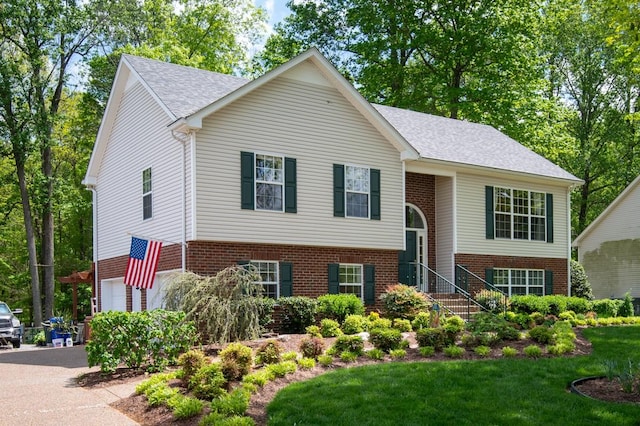 raised ranch with brick siding, a garage, a shingled roof, a front yard, and aphalt driveway