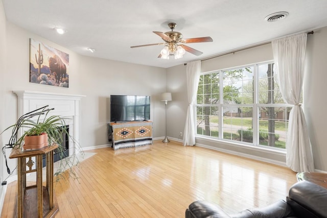 living room featuring a ceiling fan, baseboards, light wood finished floors, visible vents, and a fireplace with flush hearth