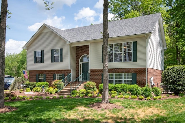 raised ranch with a shingled roof, brick siding, and a front lawn