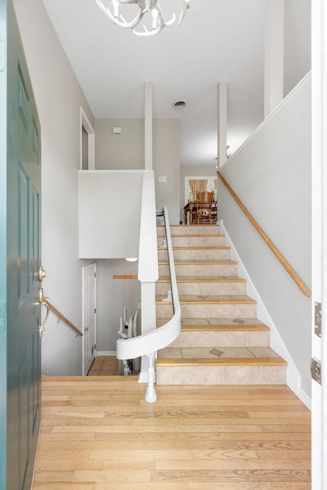 stairs featuring a notable chandelier, visible vents, and wood finished floors