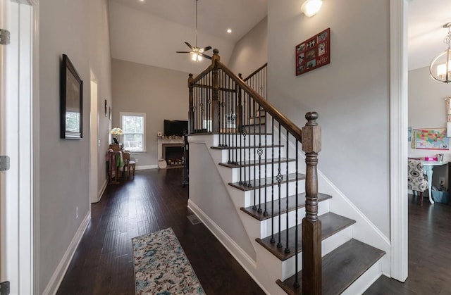 stairs featuring wood finished floors, a ceiling fan, a fireplace, baseboards, and a towering ceiling