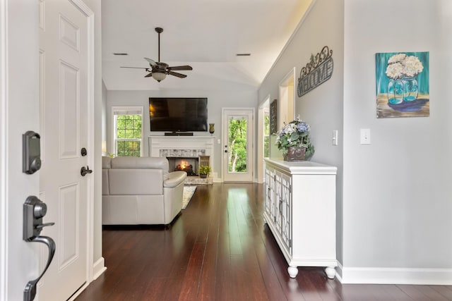 interior space with a lit fireplace, dark wood finished floors, baseboards, ceiling fan, and lofted ceiling