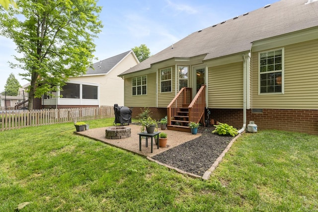 back of property featuring a yard, fence, a patio, a sunroom, and a fire pit
