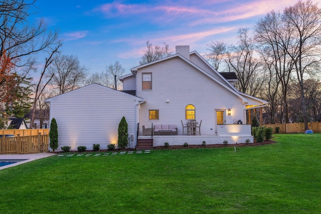 back of property at dusk featuring a chimney, a yard, brick siding, and fence