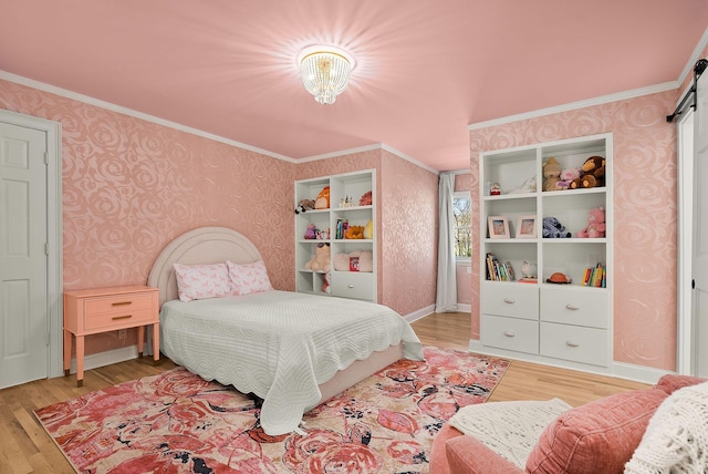 bedroom featuring light wood finished floors, wallpapered walls, a barn door, and crown molding