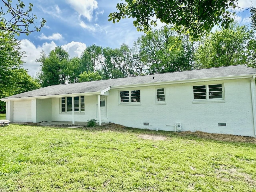 back of property featuring a lawn, an attached garage, brick siding, and crawl space