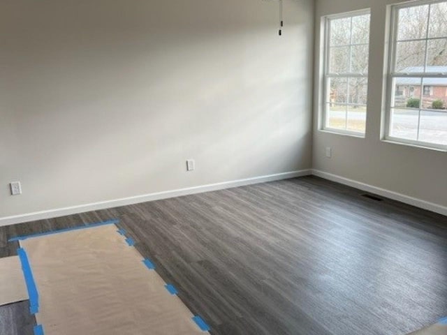empty room with dark wood-type flooring, baseboards, and visible vents