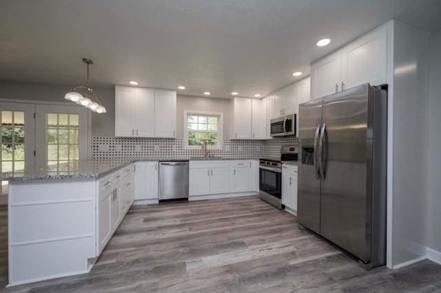 kitchen with light wood finished floors, a sink, white cabinetry, a peninsula, and stainless steel appliances