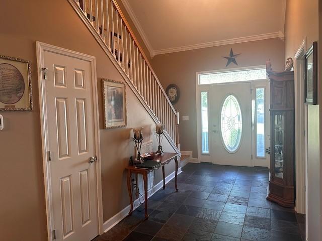 foyer with crown molding, stairs, baseboards, and stone tile floors