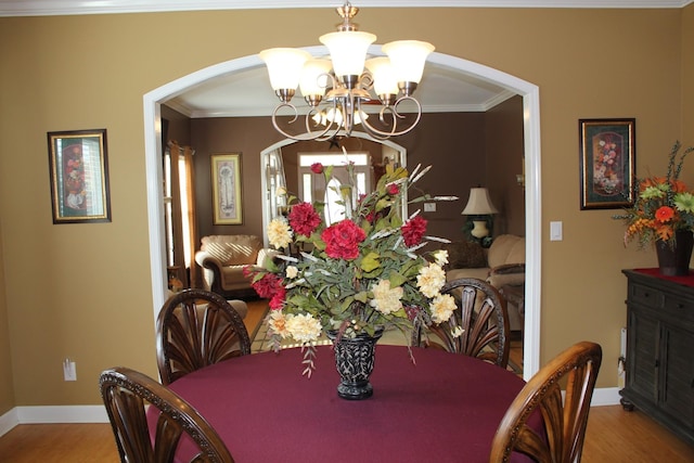 dining room with crown molding, arched walkways, a notable chandelier, and wood finished floors