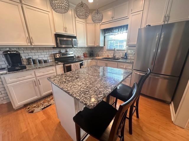 kitchen featuring light wood-style floors, stainless steel appliances, dark stone counters, and a sink