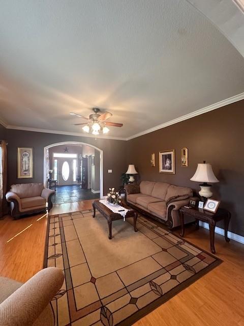 living area featuring ceiling fan, ornamental molding, arched walkways, and wood finished floors