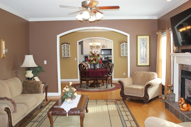 living area featuring crown molding, a fireplace, ceiling fan with notable chandelier, and arched walkways