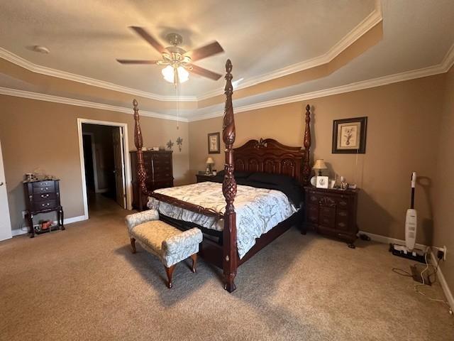 bedroom with a ceiling fan, a tray ceiling, crown molding, baseboards, and light carpet