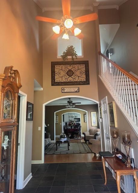 foyer with baseboards, ceiling fan, a towering ceiling, arched walkways, and stairway