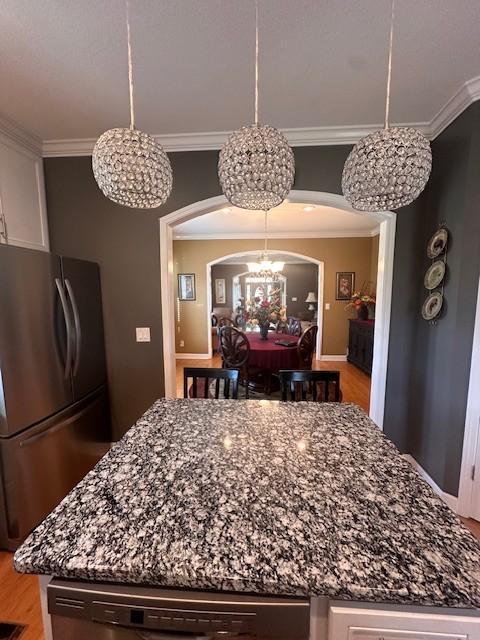 dining space featuring ornamental molding, light wood-style flooring, arched walkways, and a notable chandelier