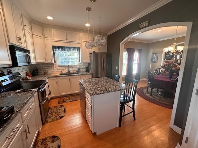 kitchen featuring a sink, stainless steel appliances, light wood finished floors, arched walkways, and a kitchen bar