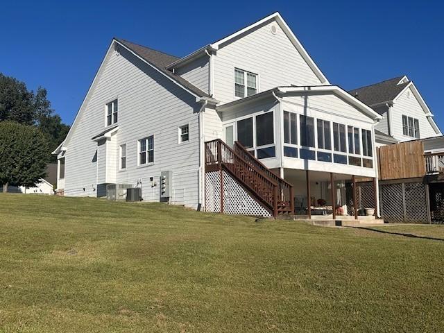 rear view of house featuring stairway, a sunroom, a yard, and a deck